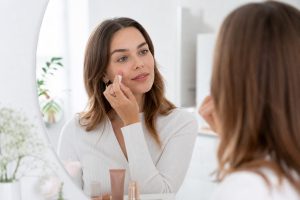 Frau trägt natürliches Make-up vor einem hellen Spiegel auf.